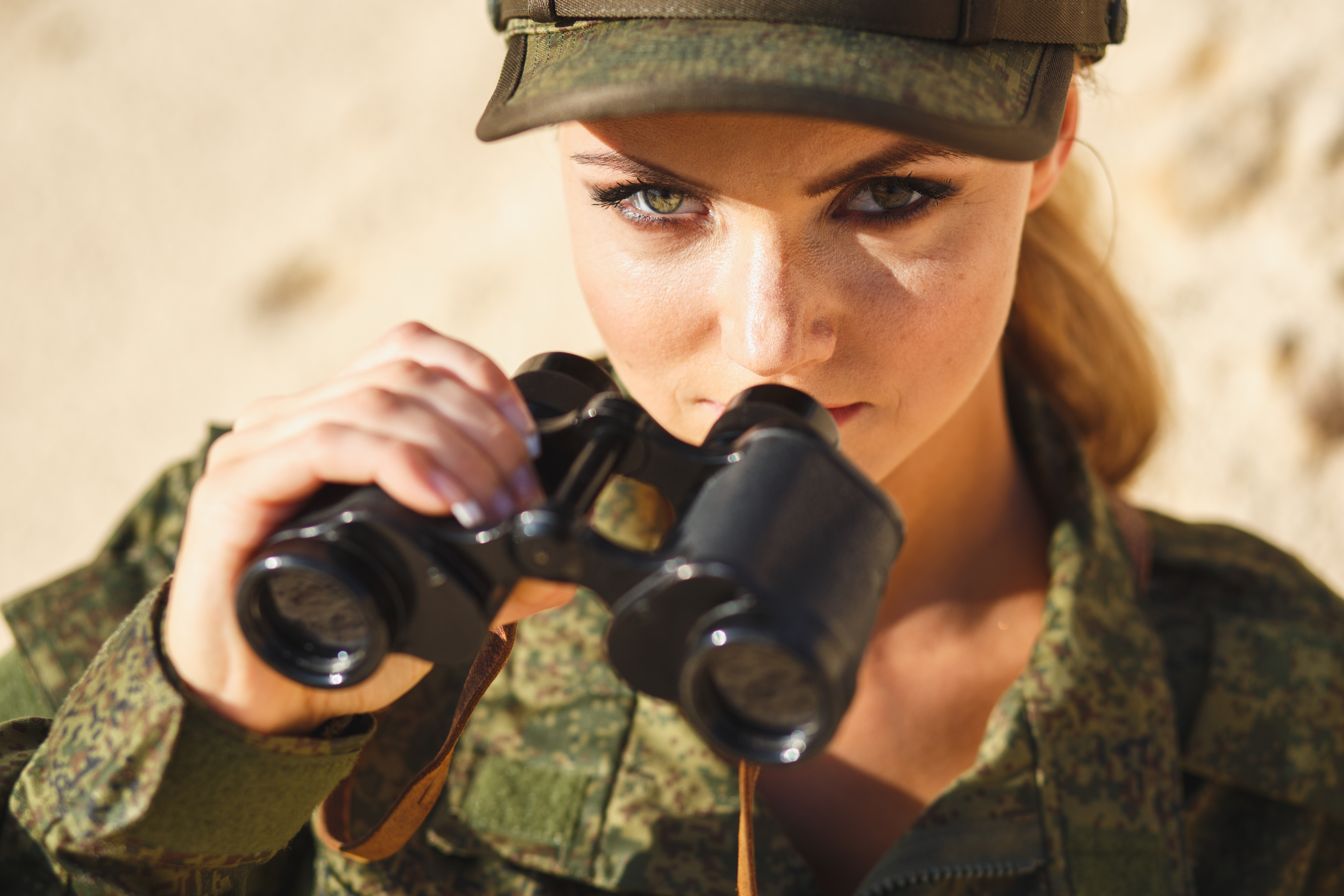 Gorgeous young woman in a Military costume with a binoculars on the background of a dessert